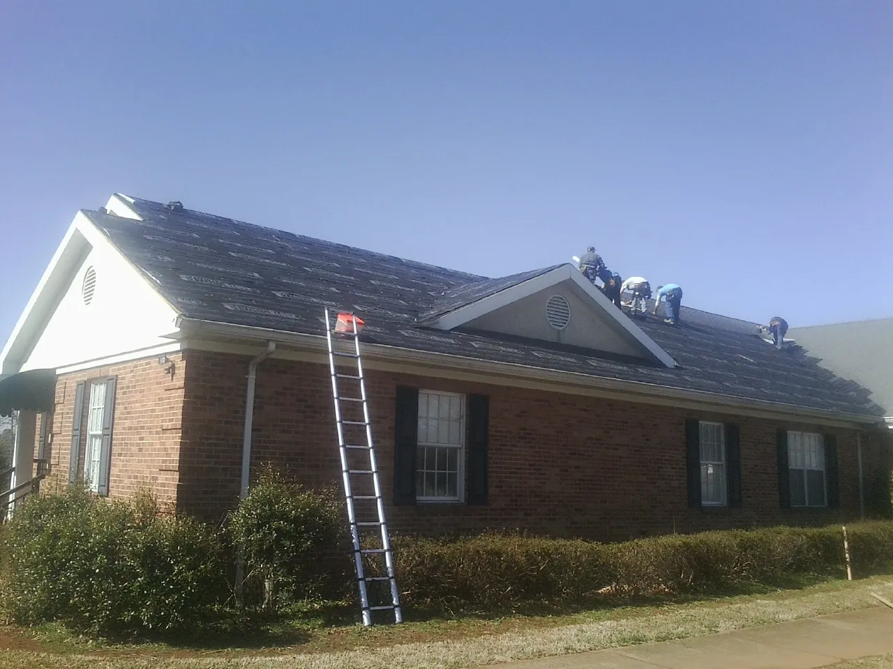 Crew tearing shingles off a brick ranch roof with a ladder set — Emergency Roof Repair work by our crew in Custer