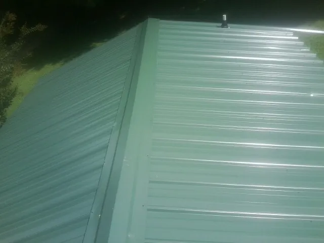New green metal panels meeting at the ridge of a roof — Flat Roof Repair work by our crew in Custer